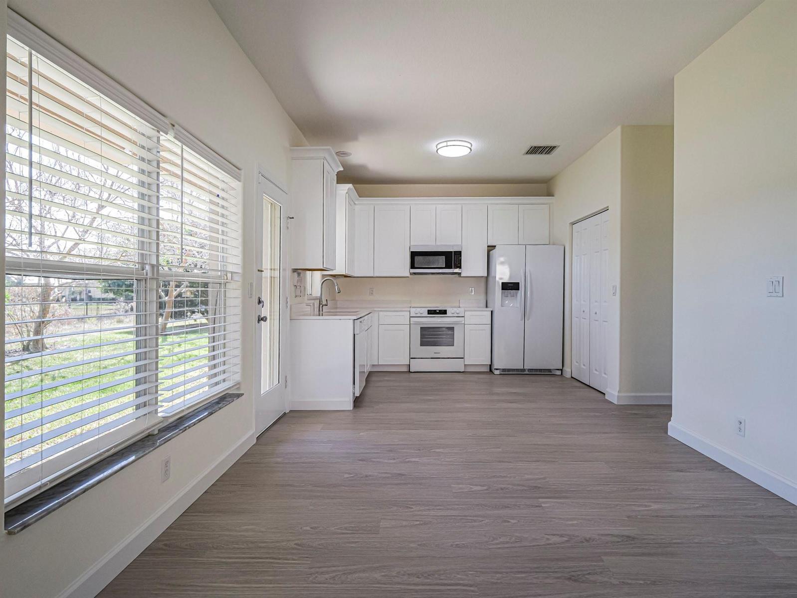 A kitchen with white cabinets, white appliances, and light wood-look flooring next to a window — 1834 77th Drive # 1834, Vero Beach FL 32966, VERO BEACH, FL