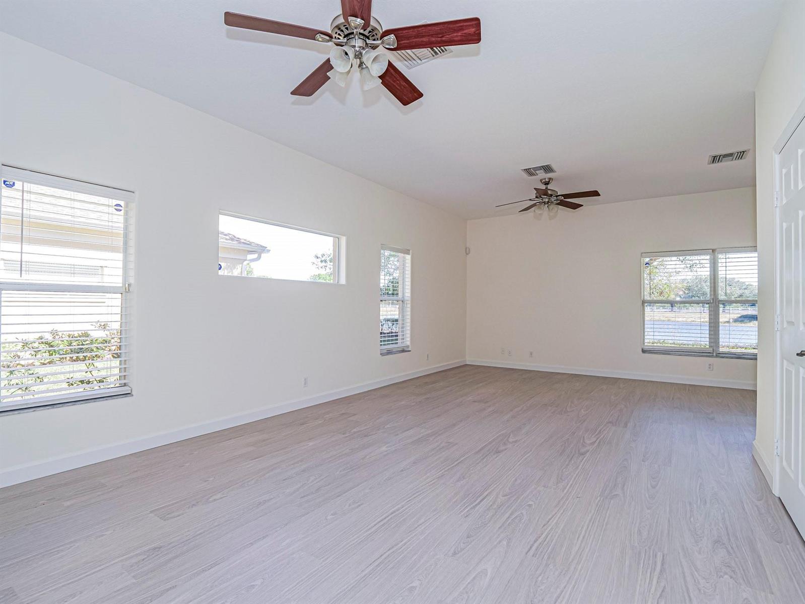 An empty room with light wood-look flooring, white walls, two ceiling fans, and multiple windows — 1834 77th Drive # 1834, Vero Beach FL 32966, VERO BEACH, FL