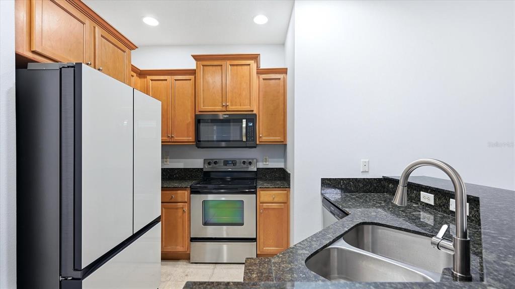 A kitchen features wood cabinets, stainless steel appliances, and dark granite countertops — 7839 LIMESTONE LANE UNIT 12-204, SARASOTA, FL