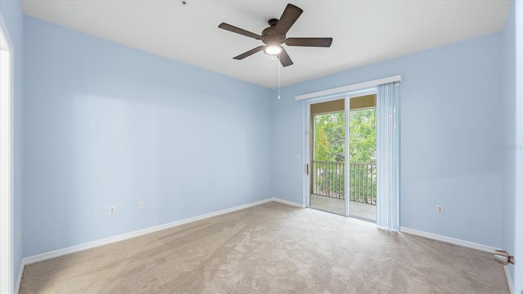 An empty bedroom with light blue walls, beige carpet, a ceiling fan, and sliding glass doors — 7839 LIMESTONE LANE UNIT 12-204, SARASOTA, FL