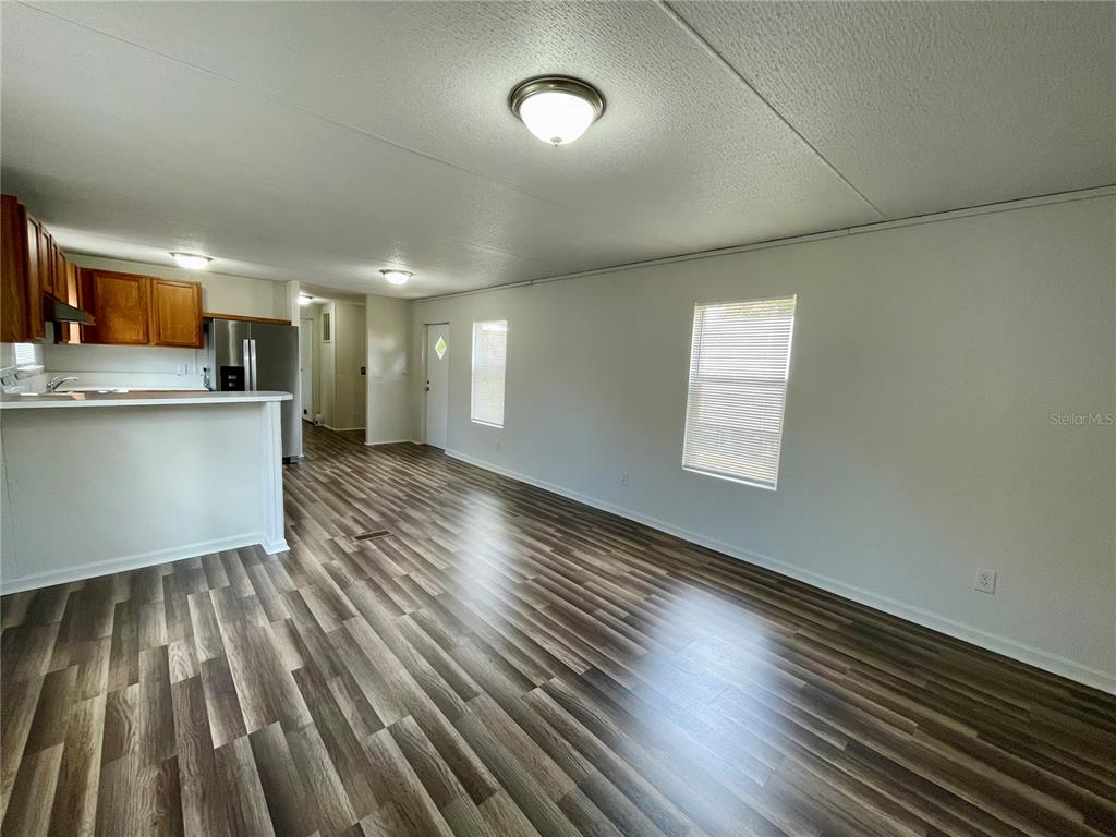 An open-concept living area features wood-look flooring, white walls, and an adjacent kitchen — 6328 EUGENE ACRES LANE, GIBSONTON, FL
