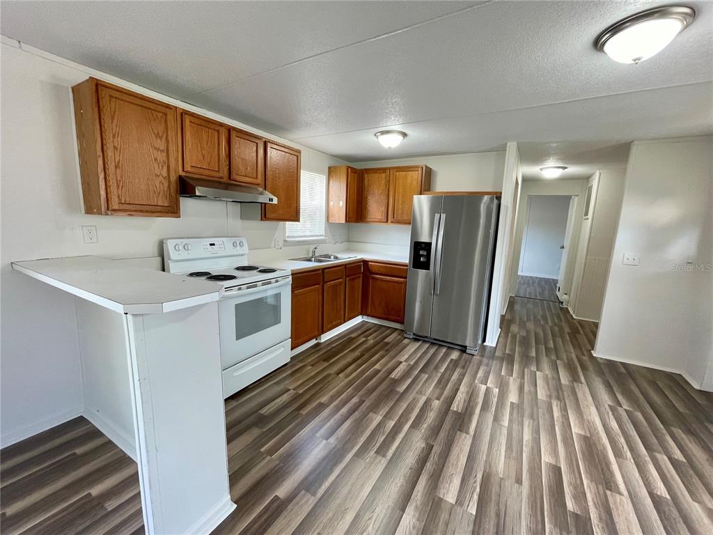 A kitchen features wood cabinets, white appliances, a stainless steel refrigerator, and wood-look flooring — 6328 EUGENE ACRES LANE, GIBSONTON, FL
