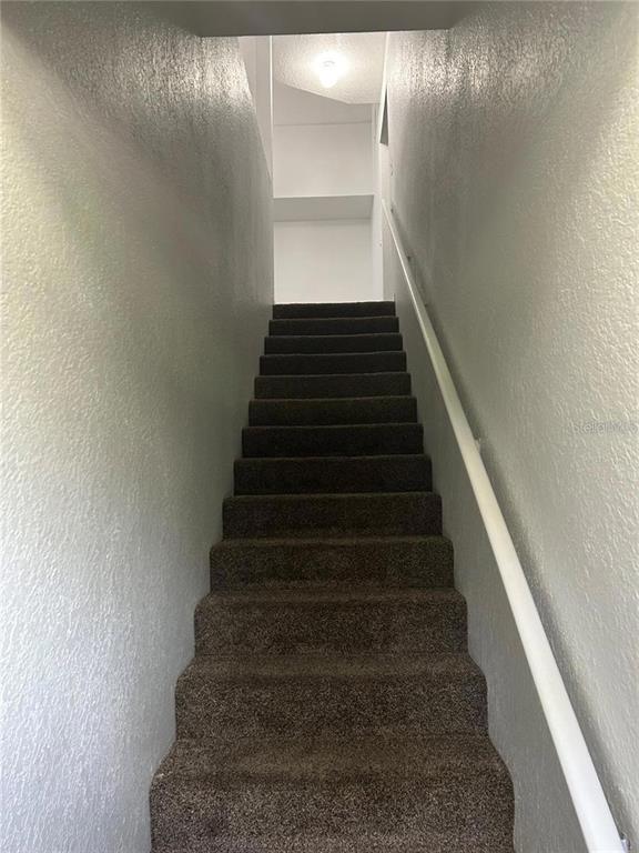 A straight staircase with dark brown carpet leads upward between two plain white walls — 6424 RALEIGH STREET UNIT 3112, ORLANDO, FL