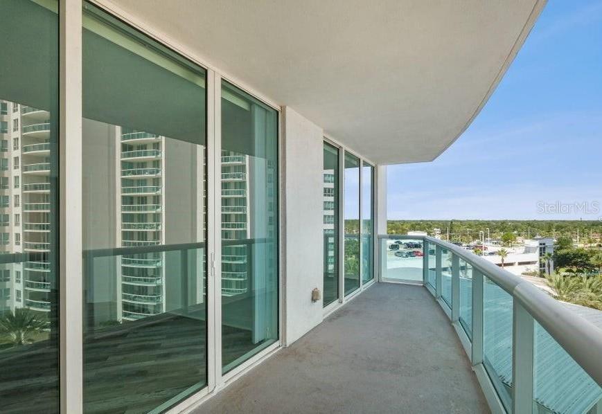 A curved balcony with glass railings overlooks a parking lot and distant trees — 231 RIVERSIDE DRIVE UNIT 708-1, HOLLY HILL, FL