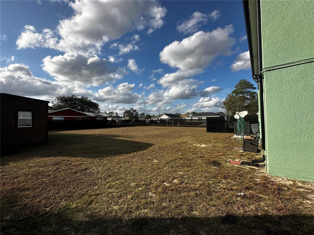 A large, grassy backyard features a fence, a small shed, and a green house exterior — 15040 SW 39TH CIRCLE, OCALA, FL