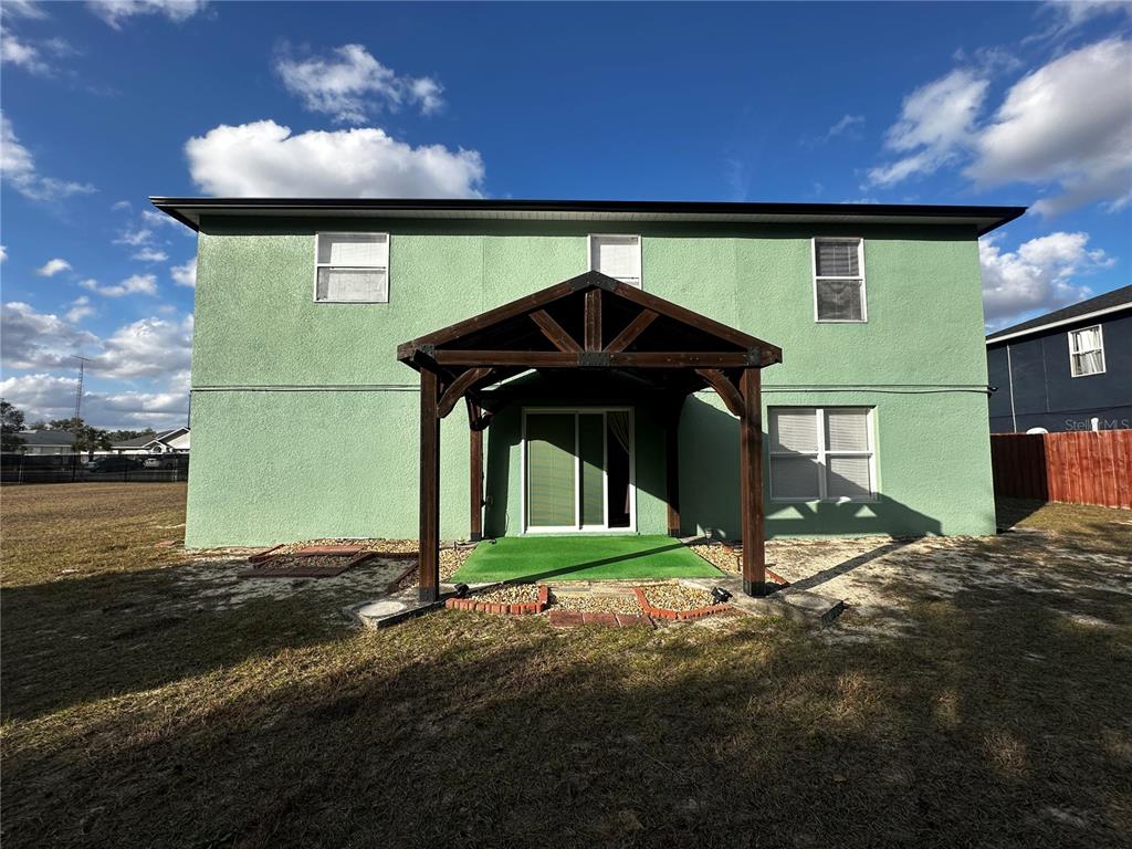 The rear exterior of a two-story green house features a wooden pergola over a patio — 15040 SW 39TH CIRCLE, OCALA, FL