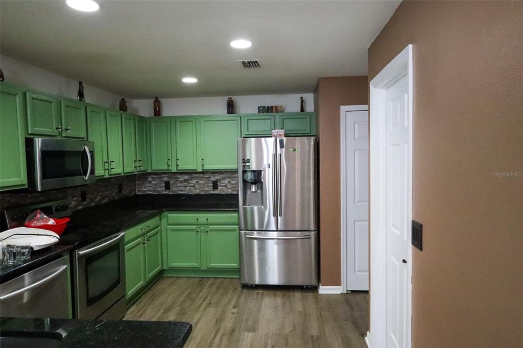 A kitchen features green cabinets, stainless steel appliances, black countertops, and wood-look flooring — 15040 SW 39TH CIRCLE, OCALA, FL