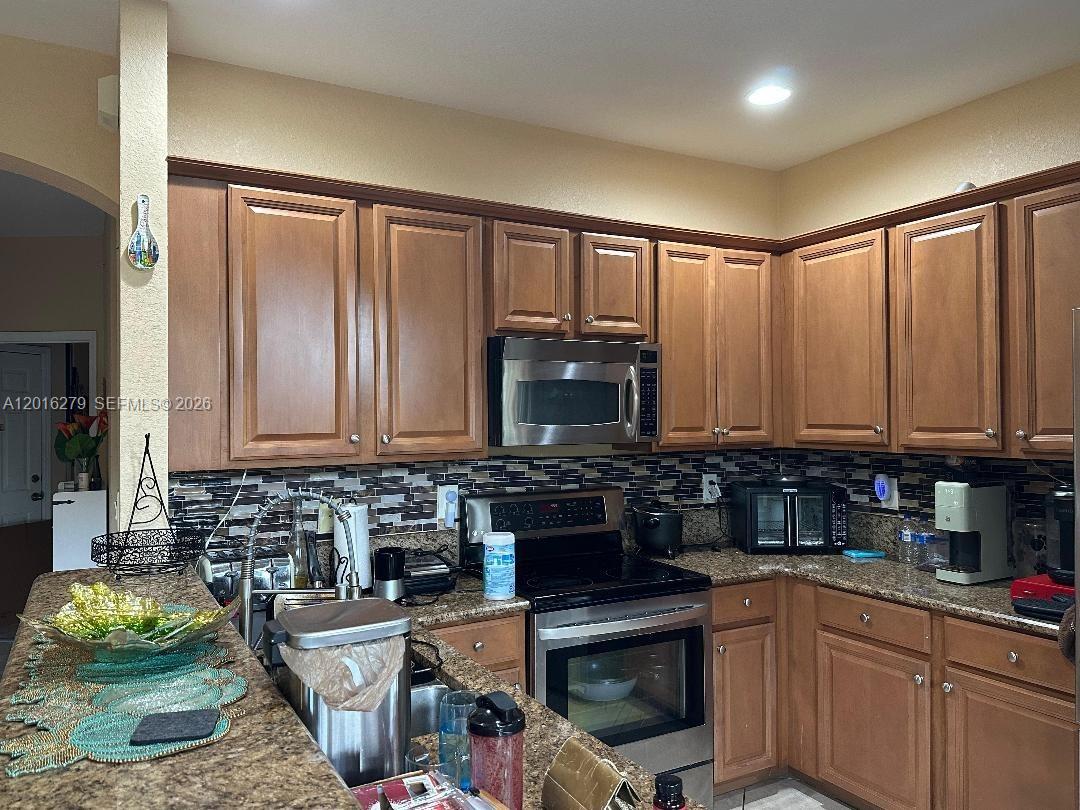 A kitchen features wood cabinets, granite countertops, stainless steel appliances, and a mosaic tile backsplash — 10361 NW 32nd Ter # 0, Doral FL 33172, DORAL, FL