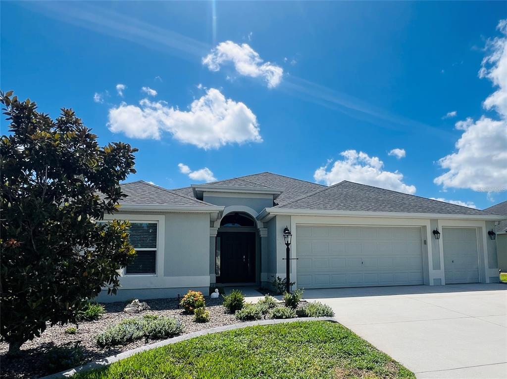 A single-story house with a gray stucco exterior, a three-car garage, and a landscaped yard — 5833 ABNEY AVENUE, THE VILLAGES, FL