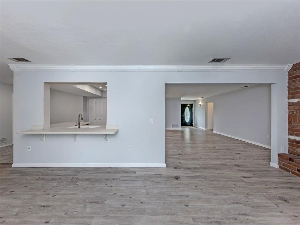 A view of a room with light gray walls, wood-look flooring, and a kitchen pass-through — 1720 SANDY COURT, VENICE, FL
