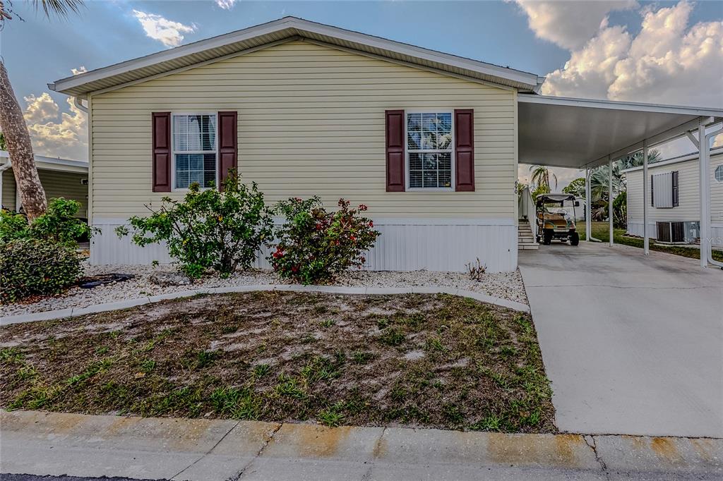 A light yellow manufactured home features brown shutters, a concrete driveway, and a covered carport — 2100 KINGS HIGHWAY UNIT 690, PORT CHARLOTTE, FL