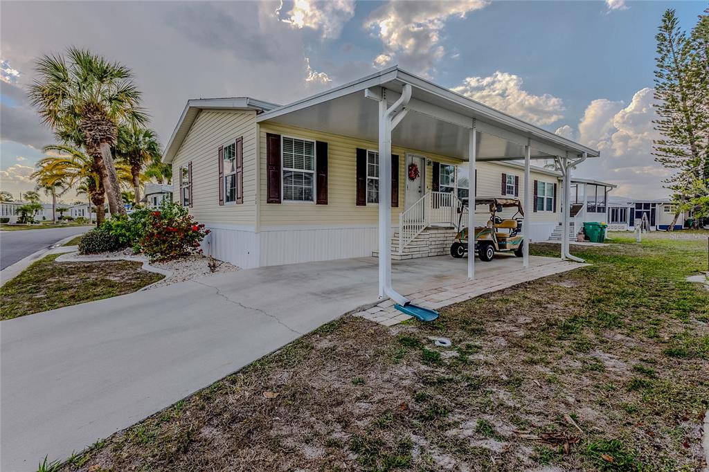 A single-story manufactured home with a carport, driveway, and palm trees under a cloudy sky — 2100 KINGS HIGHWAY UNIT 690, PORT CHARLOTTE, FL