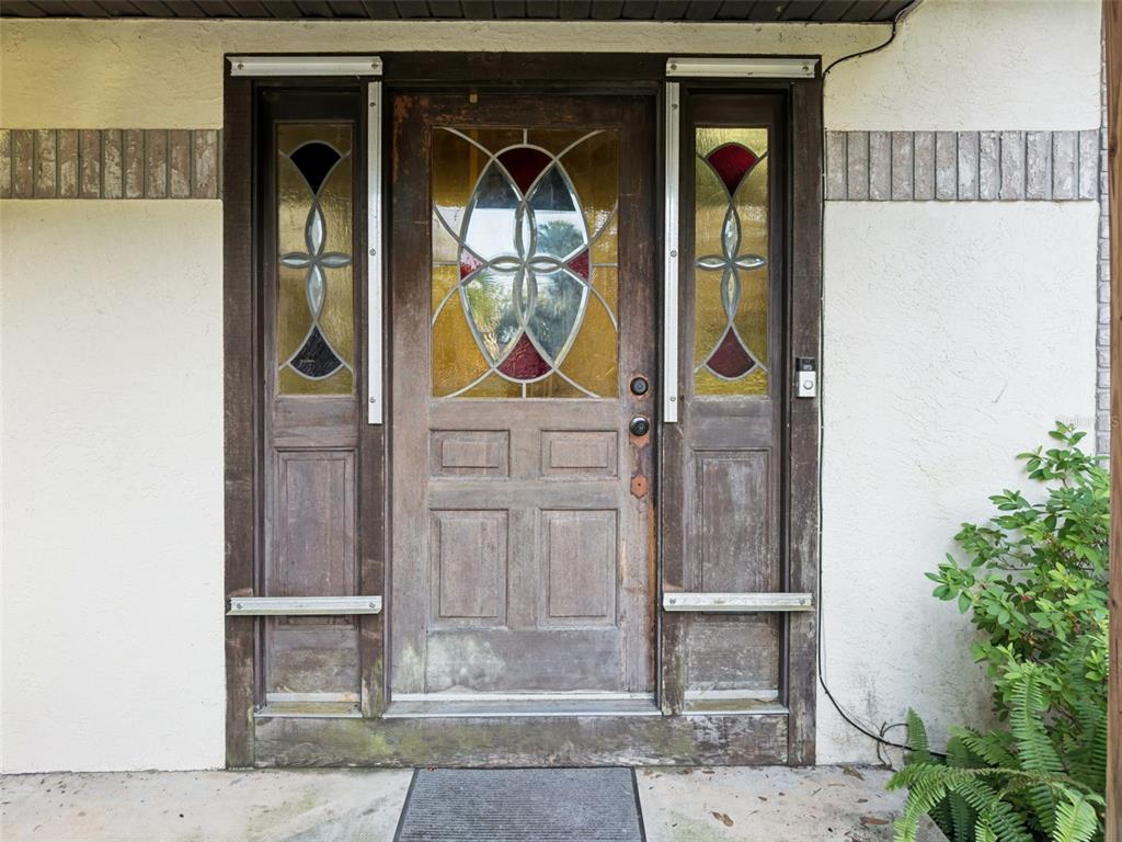 A weathered wooden front door with stained glass panels is flanked by matching sidelights — 3443 PARKLAND STREET, TITUSVILLE, FL