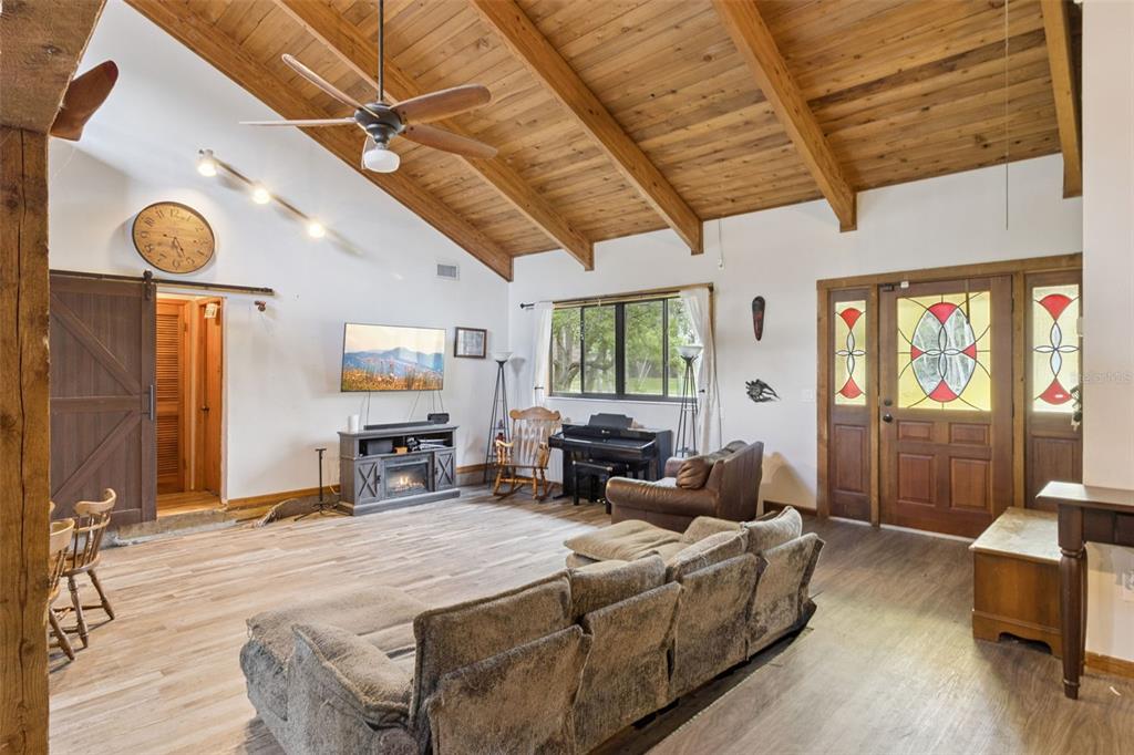 A living room features a vaulted wood-beam ceiling, wood-look flooring, a fireplace, and stained-glass doors — 3443 PARKLAND STREET, TITUSVILLE, FL