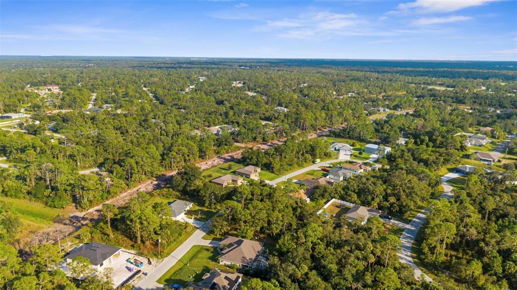 An aerial view shows a residential neighborhood with scattered houses surrounded by dense green trees — 18 BECKWITH AVENUE, NORTH PORT, FL