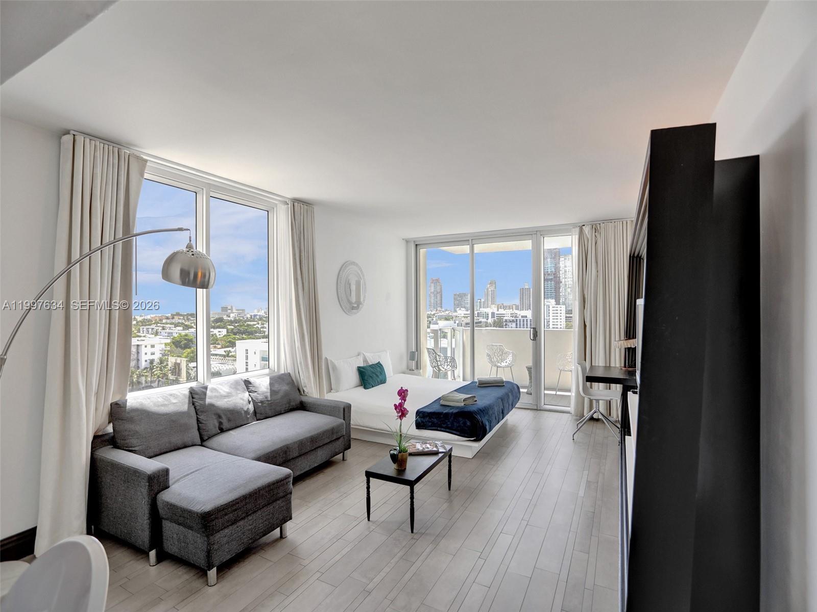 A modern studio apartment features a gray sectional sofa, a bed, and a balcony view — 1100 West Ave # 1101, Miami Beach FL 33139, MIAMI BEACH, FL