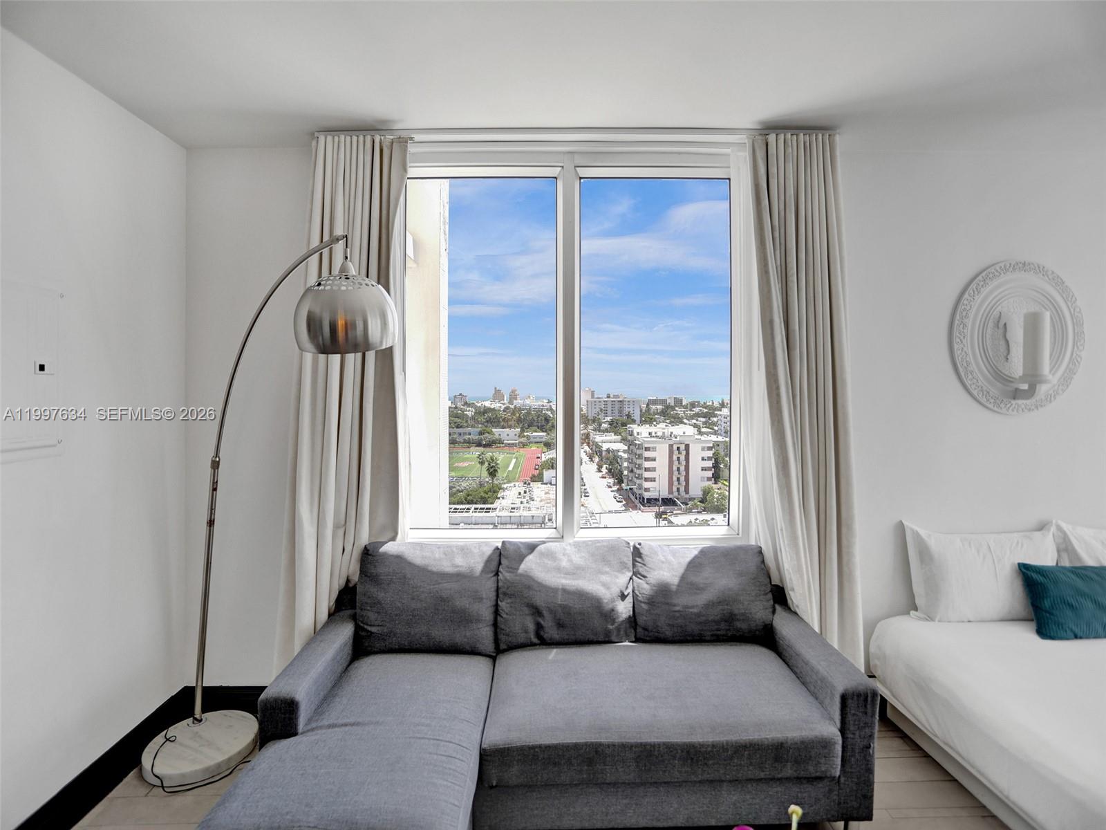 A gray sectional sofa sits before a large window with a city view and curtains — 1100 West Ave # 1101, Miami Beach FL 33139, MIAMI BEACH, FL