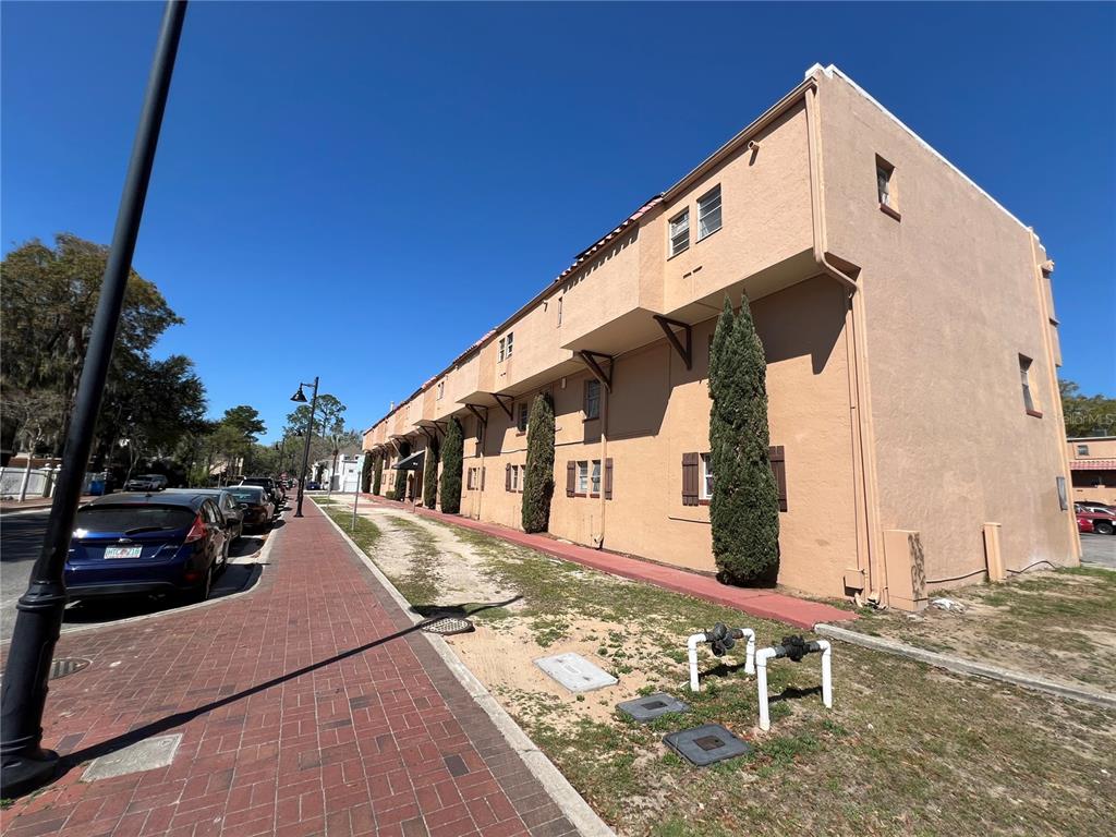 A three-story tan stucco apartment building sits beside a brick sidewalk and parked cars — 914 SW 8TH AVENUE UNIT 44, GAINESVILLE, FL
