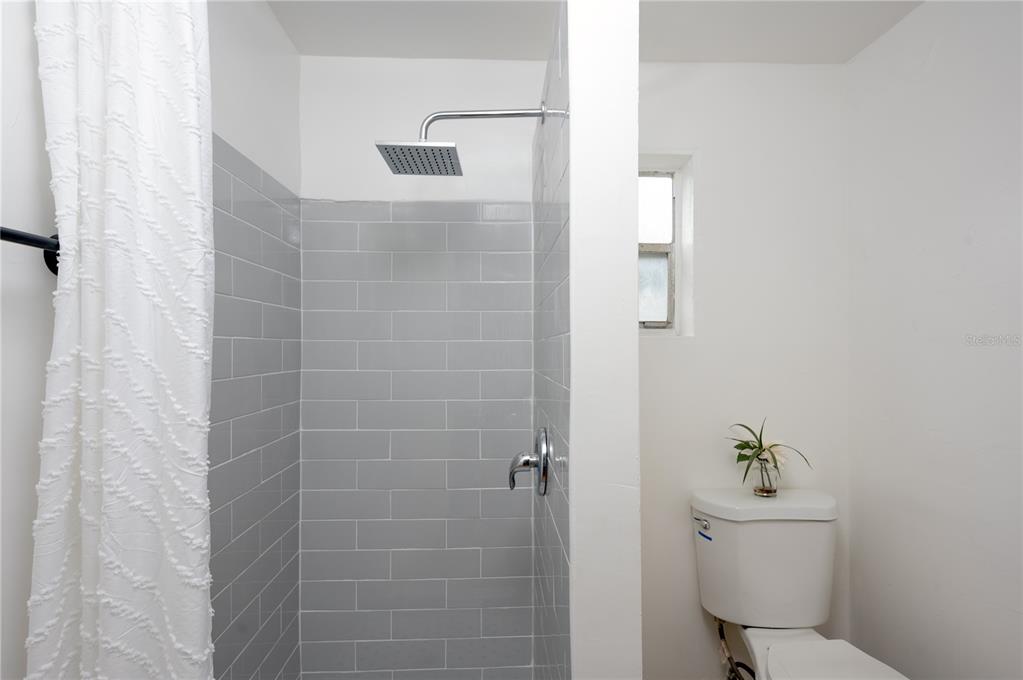 A bathroom features a walk-in shower with gray subway tile and an adjacent white toilet — 1701 S 14TH UNIT A, ST PETERSBURG, FL