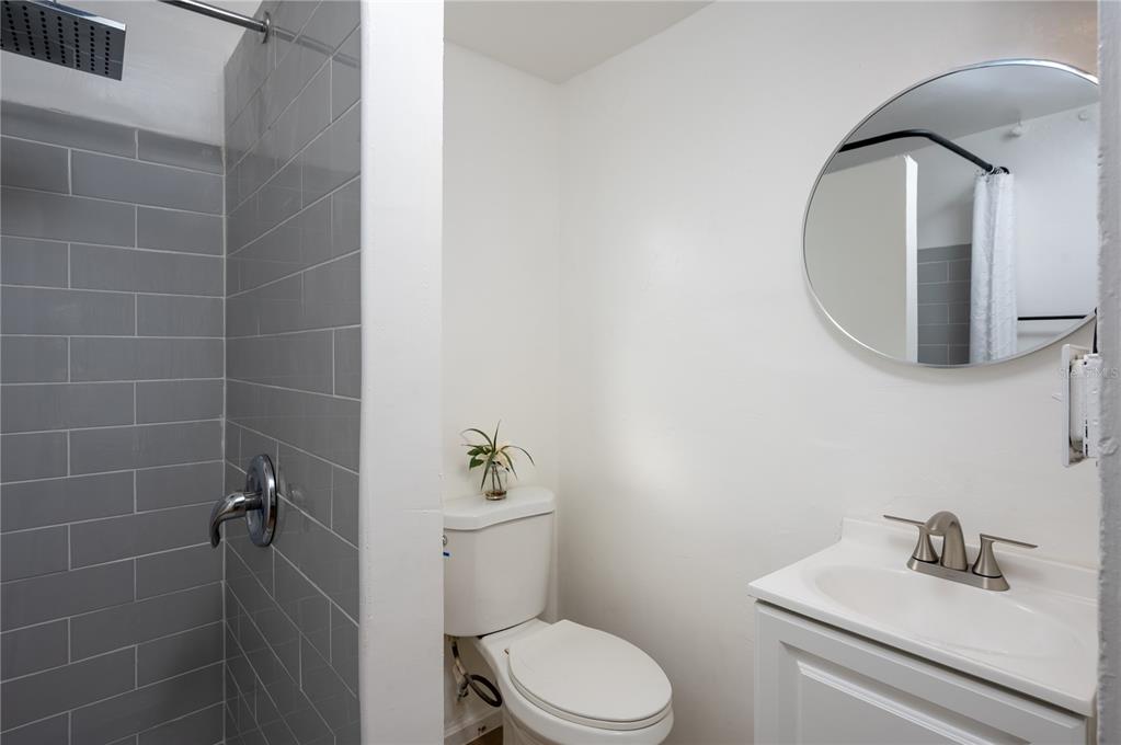A bathroom features a gray tiled shower, a white toilet, and a vanity with a mirror — 1701 S 14TH UNIT A, ST PETERSBURG, FL