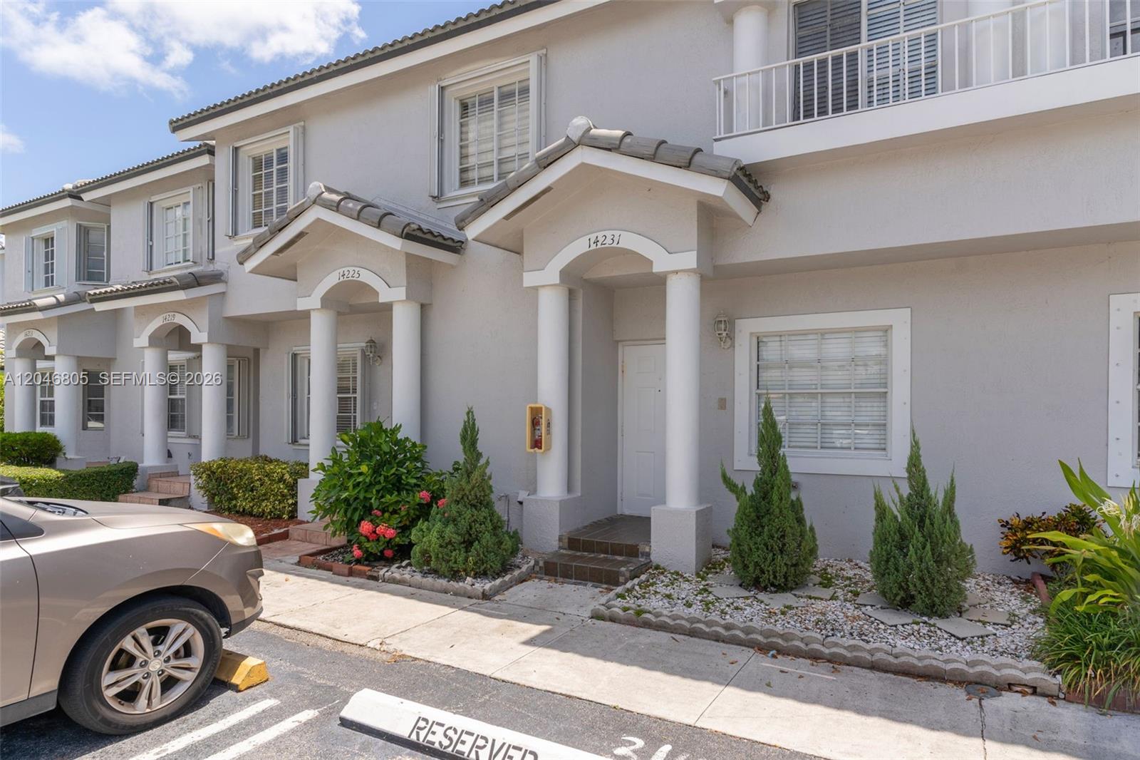The exterior of a two-story townhouse features a white facade, columns, and small landscaped gardens — 14231 SW 120th Ct # 11, Miami FL 33186, MIAMI, FL