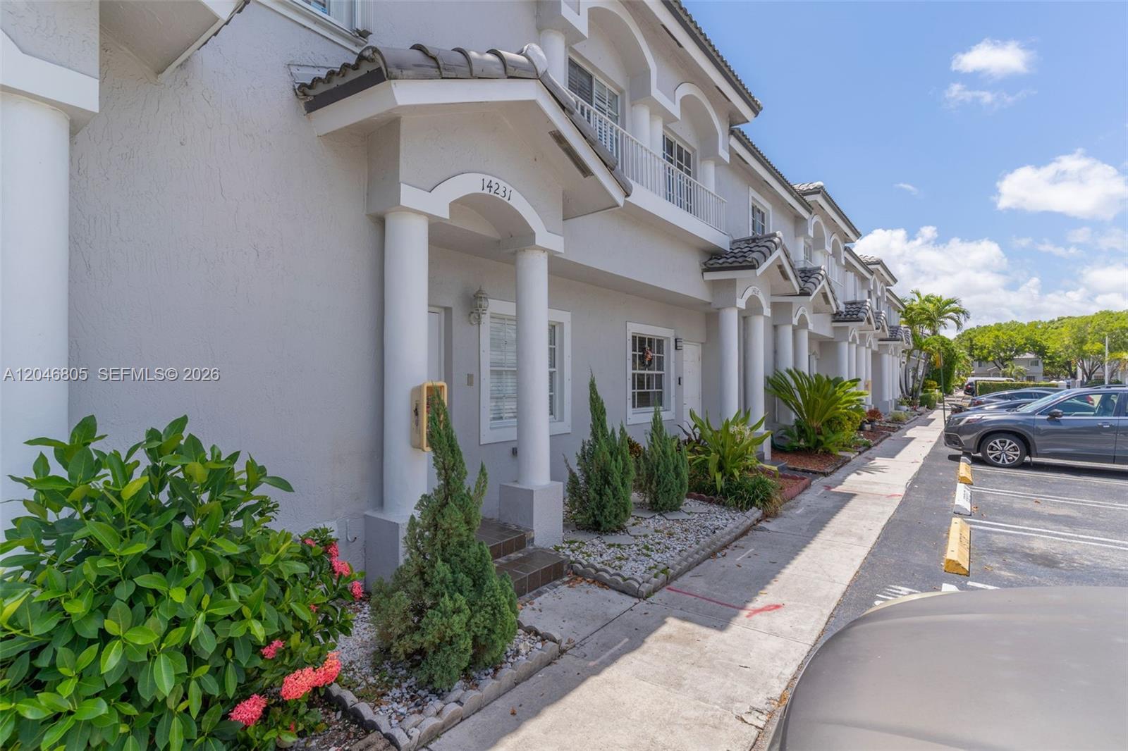 The exterior of a multi-unit townhouse complex features light gray stucco walls and arched entryways — 14231 SW 120th Ct # 11, Miami FL 33186, MIAMI, FL