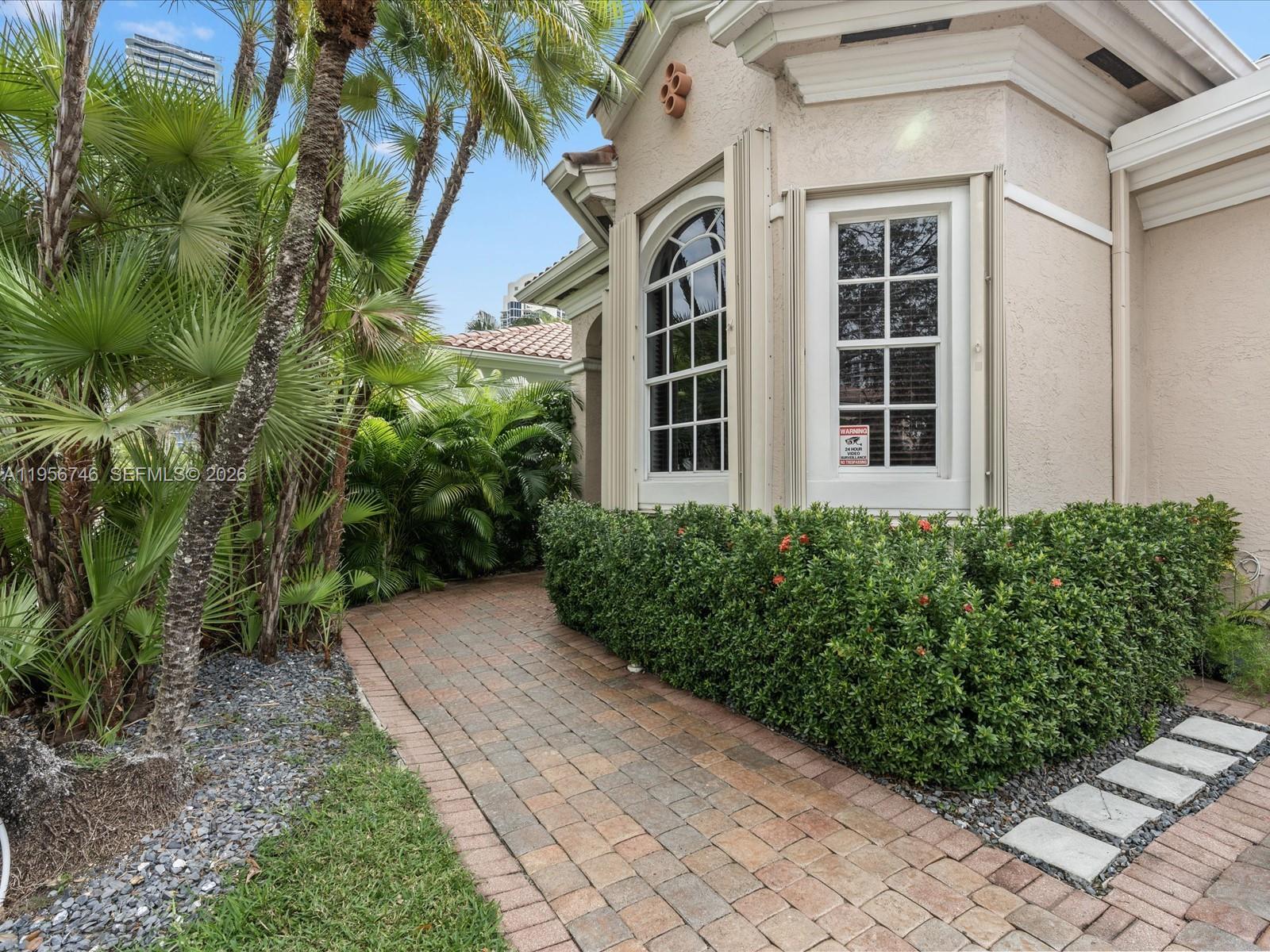 A brick walkway leads past a landscaped hedge toward the side of a stucco house — 3960 194th Trl, Sunny Isles Beach FL 33160, SUNNY ISLES BEACH, FL