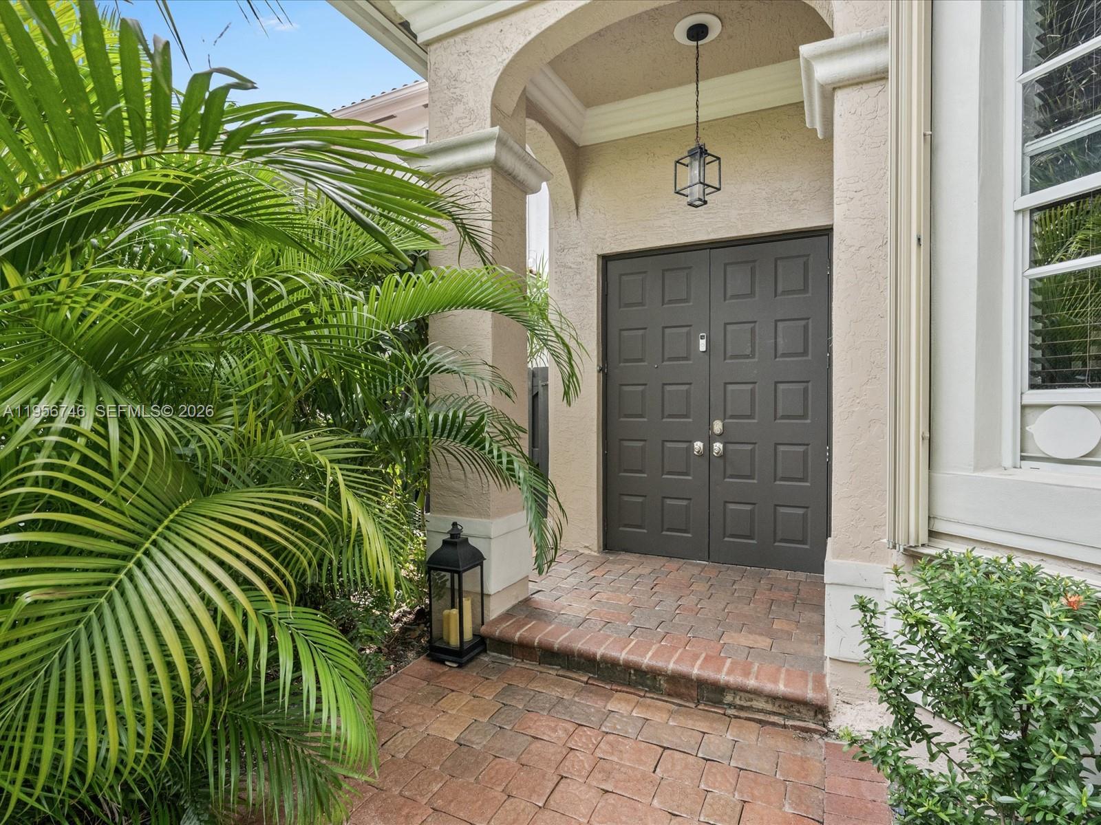 A dark double door entrance features a brick porch, a hanging lantern, and palm foliage — 3960 194th Trl, Sunny Isles Beach FL 33160, SUNNY ISLES BEACH, FL
