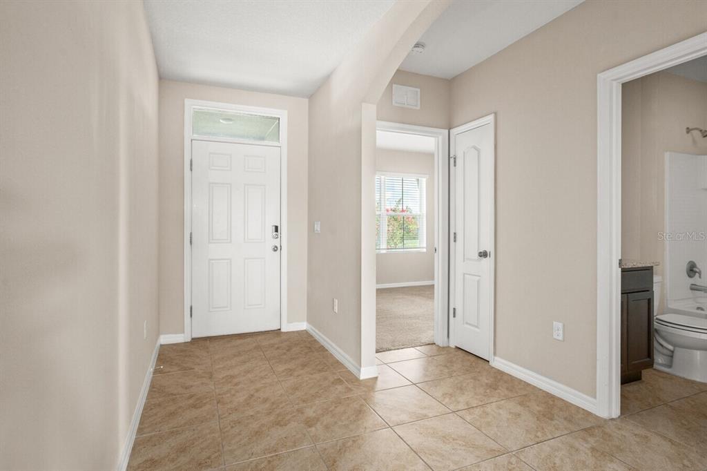 An entryway features tan tile flooring, a white front door, and access to a bathroom — 1112 FOX PATH, DAVENPORT, FL