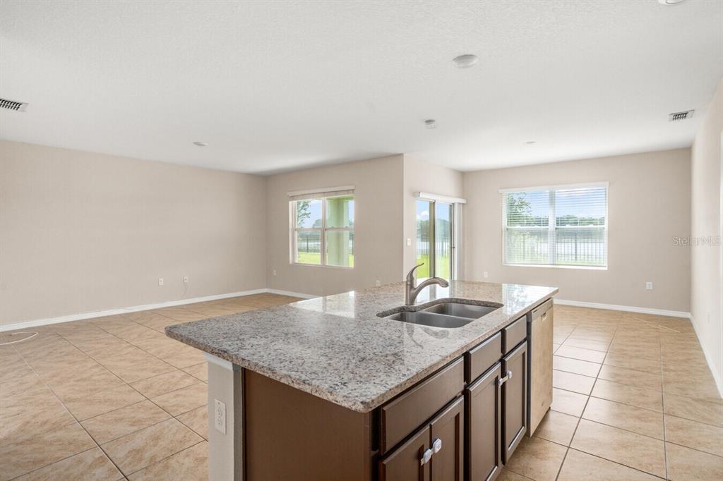 A kitchen island with granite countertops sits in an open-concept room with tile flooring — 1112 FOX PATH, DAVENPORT, FL