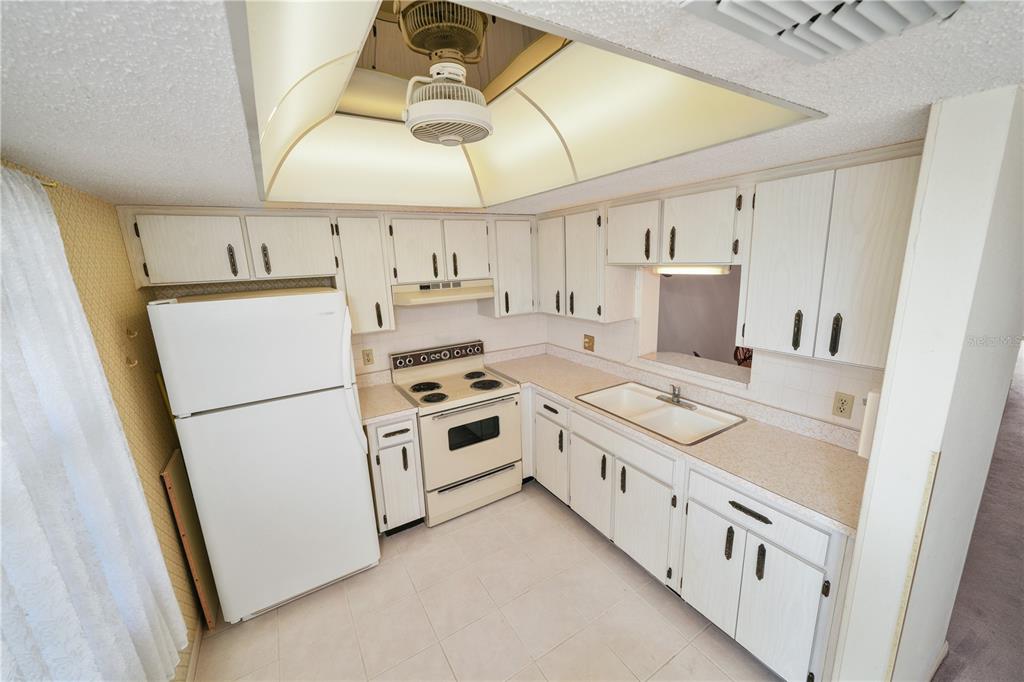 A kitchen features white cabinets, a white refrigerator, an electric stove, and a tray ceiling — 1450 HEATHER RIDGE BOULEVARD UNIT 307, DUNEDIN, FL