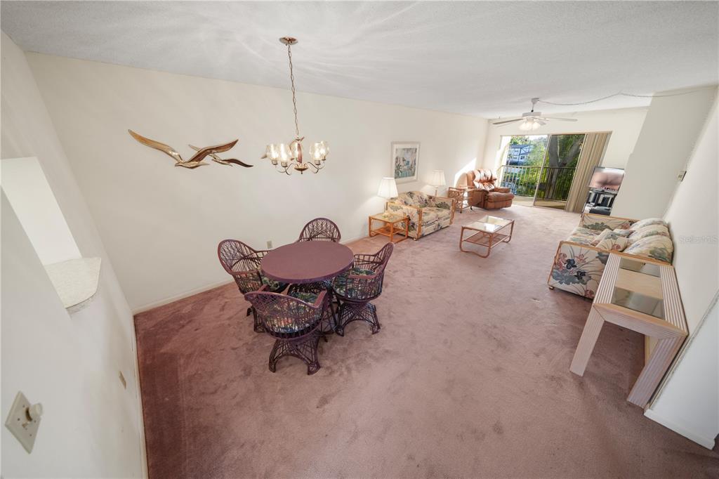 A carpeted living and dining area features wicker furniture, a chandelier, and a sliding glass door — 1450 HEATHER RIDGE BOULEVARD UNIT 307, DUNEDIN, FL