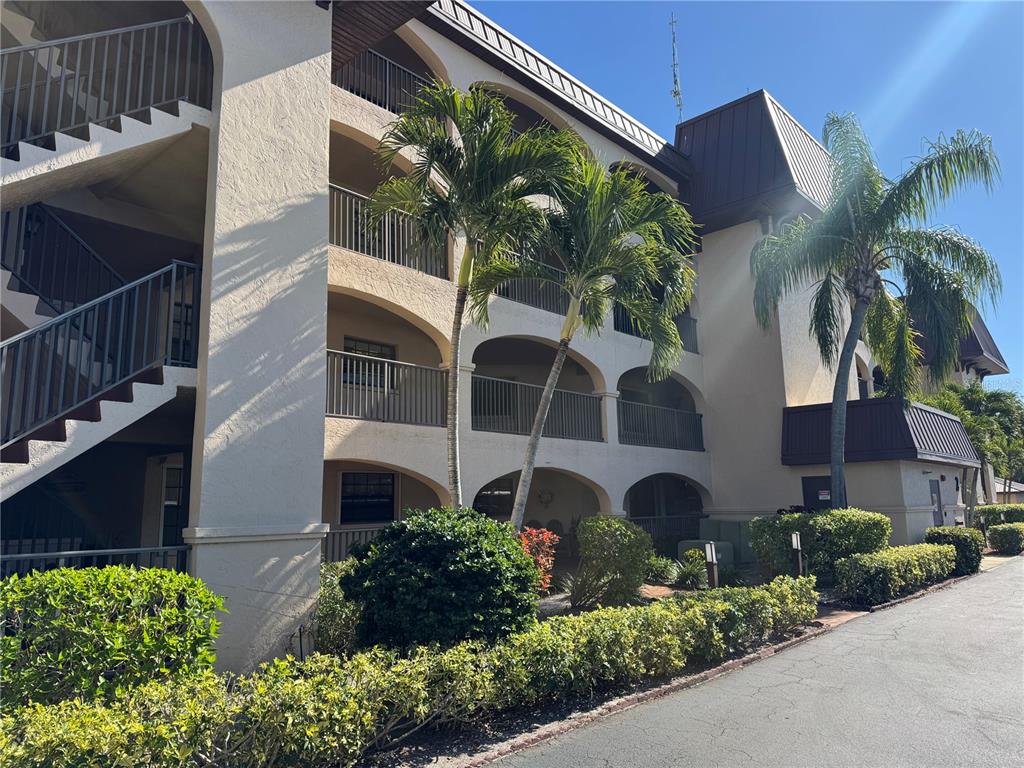 A multi-story apartment building features arched balconies, exterior staircases, and surrounding palm trees and landscaping — 23465 HARBORVIEW ROAD UNIT 244, PUNTA GORDA, FL
