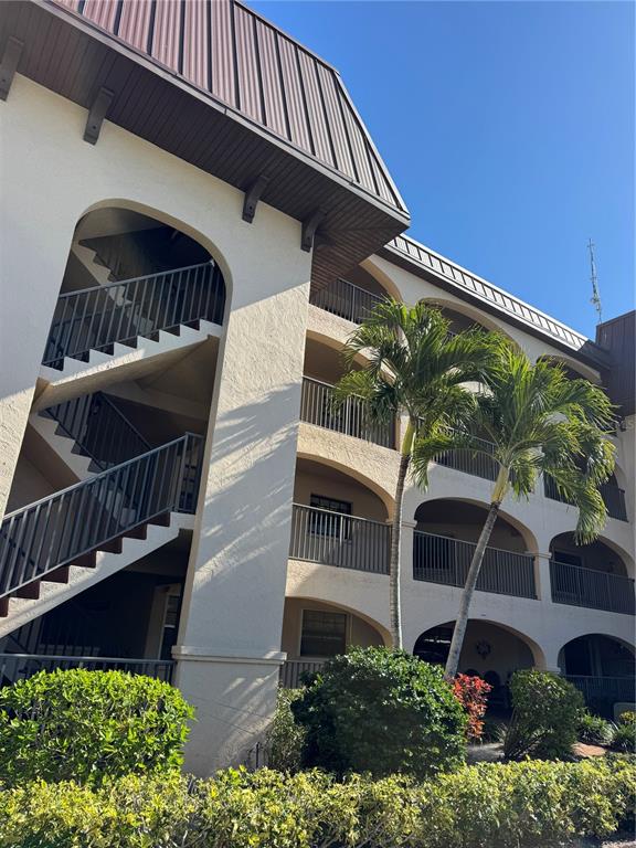 A multi-story apartment building features exterior staircases, arched balconies, and palm trees — 23465 HARBORVIEW ROAD UNIT 244, PUNTA GORDA, FL