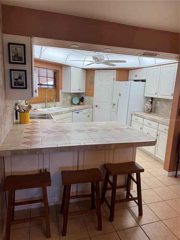 A kitchen features white cabinets, a tiled breakfast bar, and three wooden bar stools — 23465 HARBORVIEW ROAD UNIT 244, PUNTA GORDA, FL