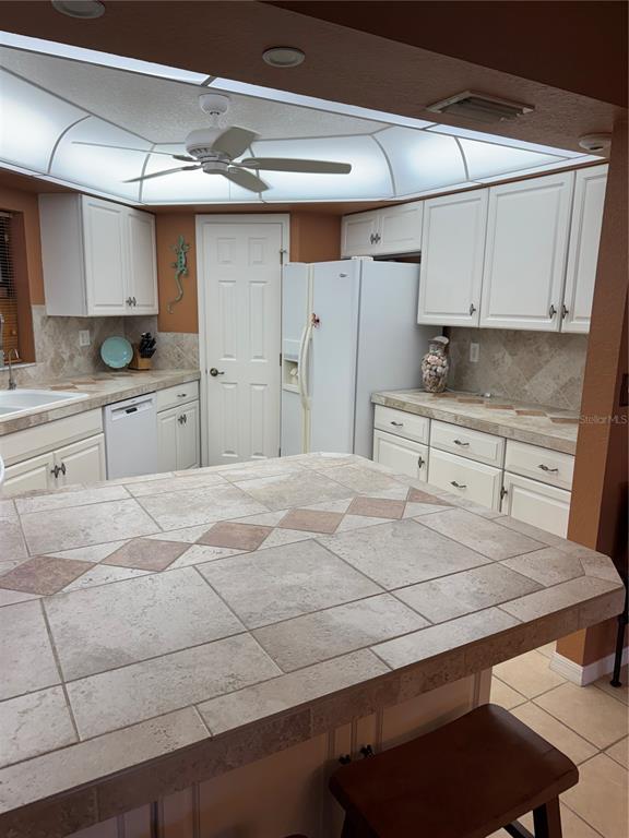 A kitchen features white cabinets, tiled countertops, a central island, and a recessed ceiling light — 23465 HARBORVIEW ROAD UNIT 244, PUNTA GORDA, FL