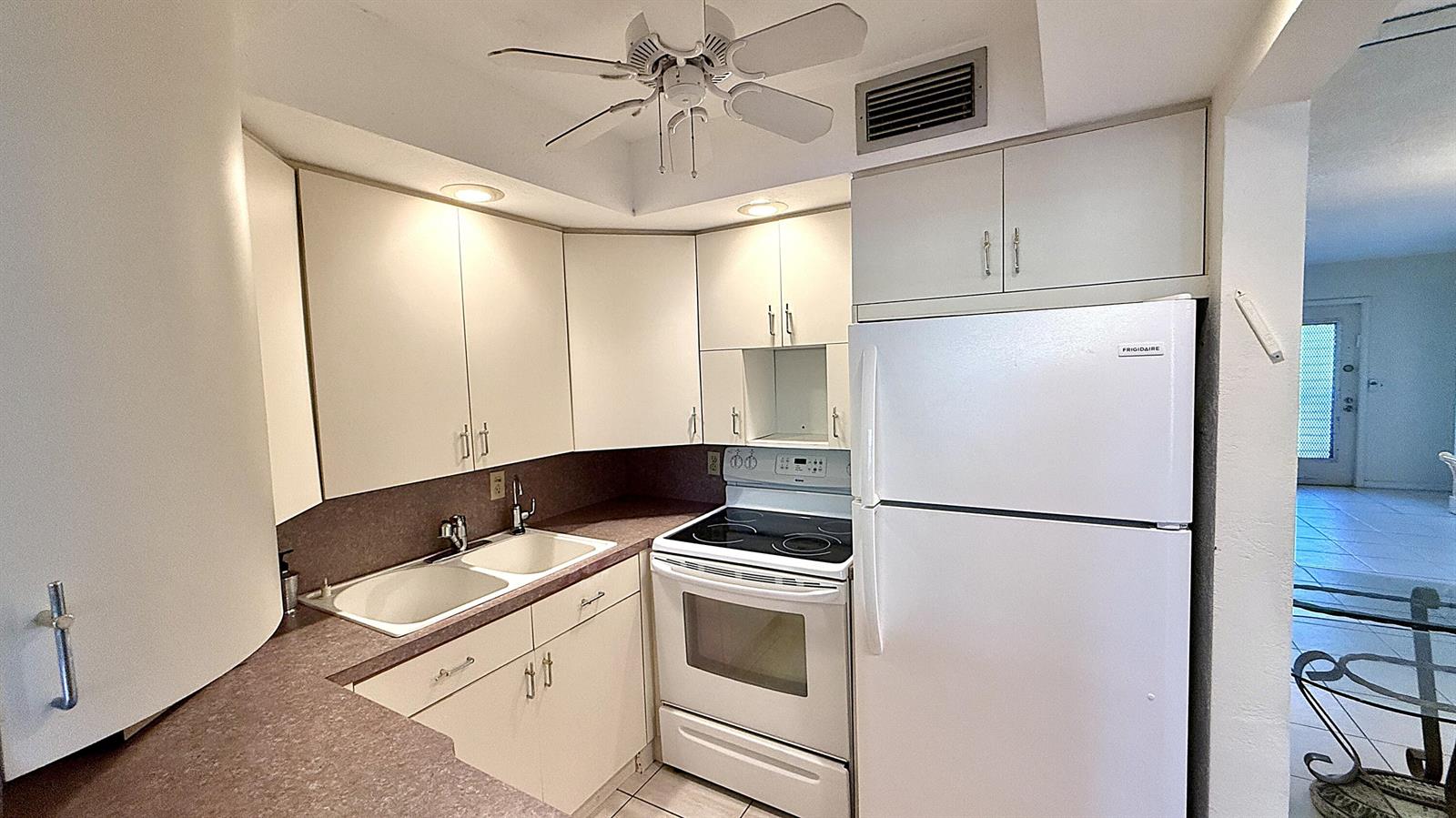A kitchen features white cabinets, white appliances, and a dark countertop with a double sink — 2009 Berkshire A, Deerfield Beach FL 33442, DEERFIELD BEACH, FL