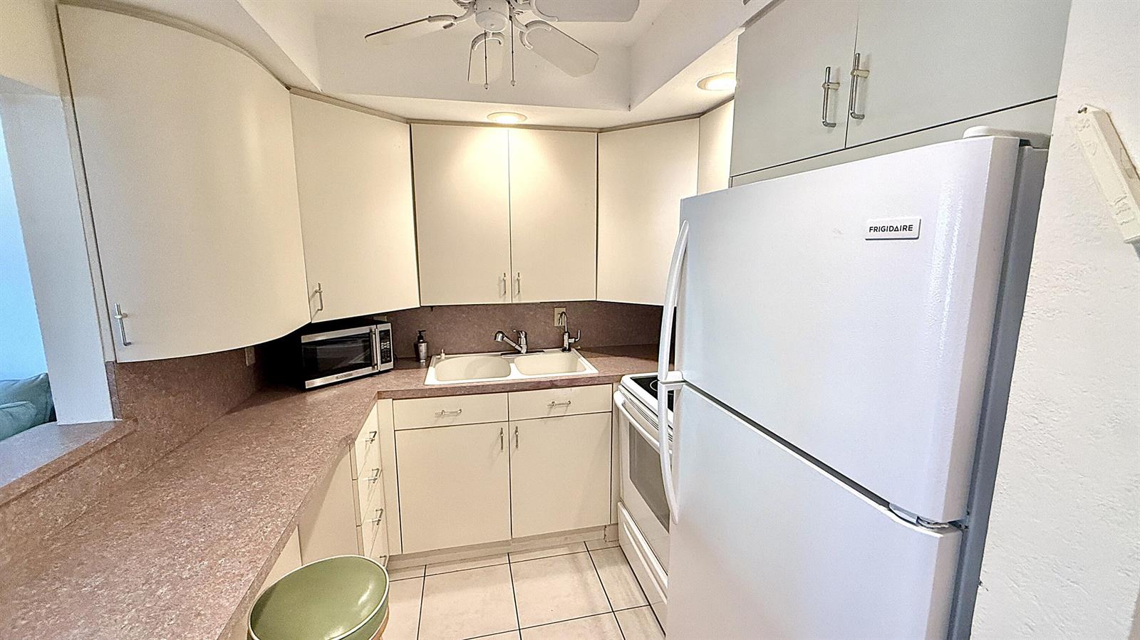 A small kitchen features white cabinets, a white refrigerator, and a pink laminate countertop — 2009 Berkshire A, Deerfield Beach FL 33442, DEERFIELD BEACH, FL