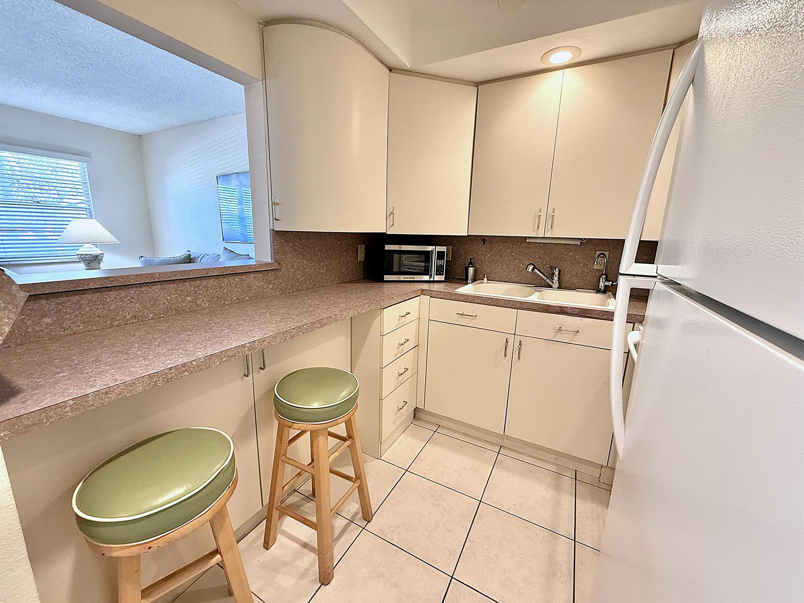 A small kitchen features beige cabinets, speckled countertops, a breakfast bar, and two green stools — 2009 Berkshire A, Deerfield Beach FL 33442, DEERFIELD BEACH, FL