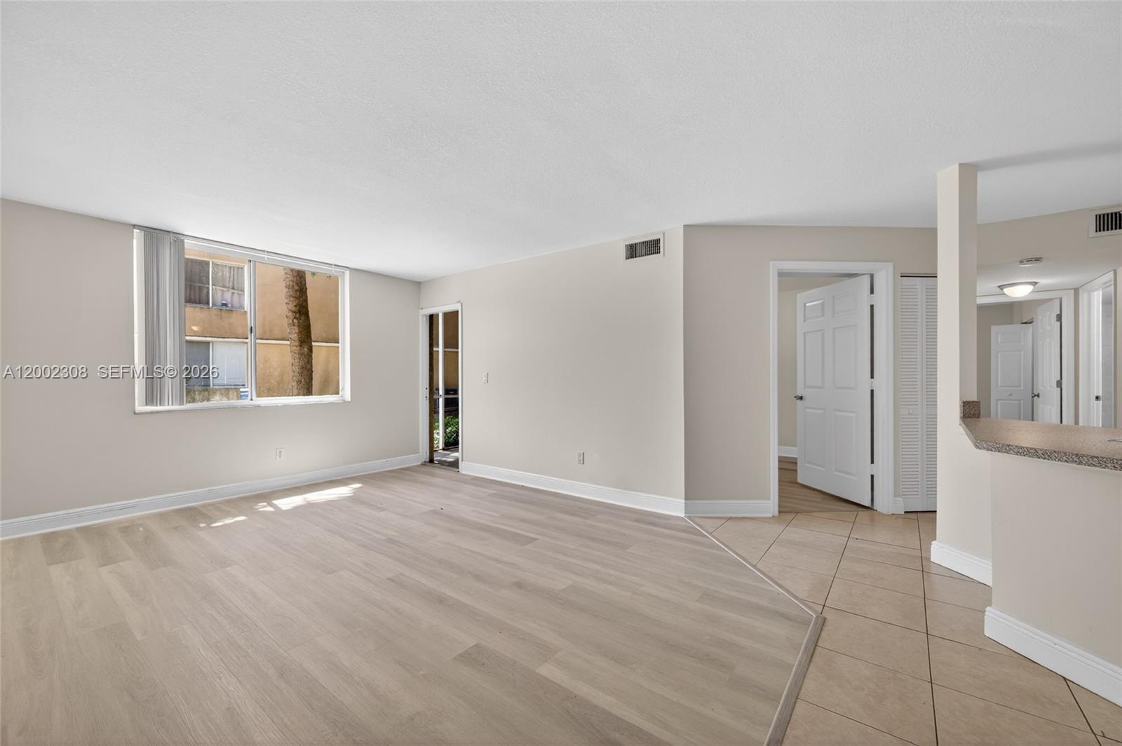An empty living room features light wood-look flooring, beige walls, and a large window — 4025 W Mcnab Rd # E109, Pompano Beach FL 33069, POMPANO BEACH, FL