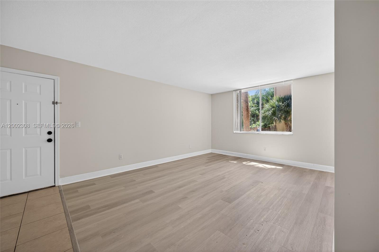 An empty room features light-colored walls, wood-look flooring, a white door, and a large window — 4025 W Mcnab Rd # E109, Pompano Beach FL 33069, POMPANO BEACH, FL