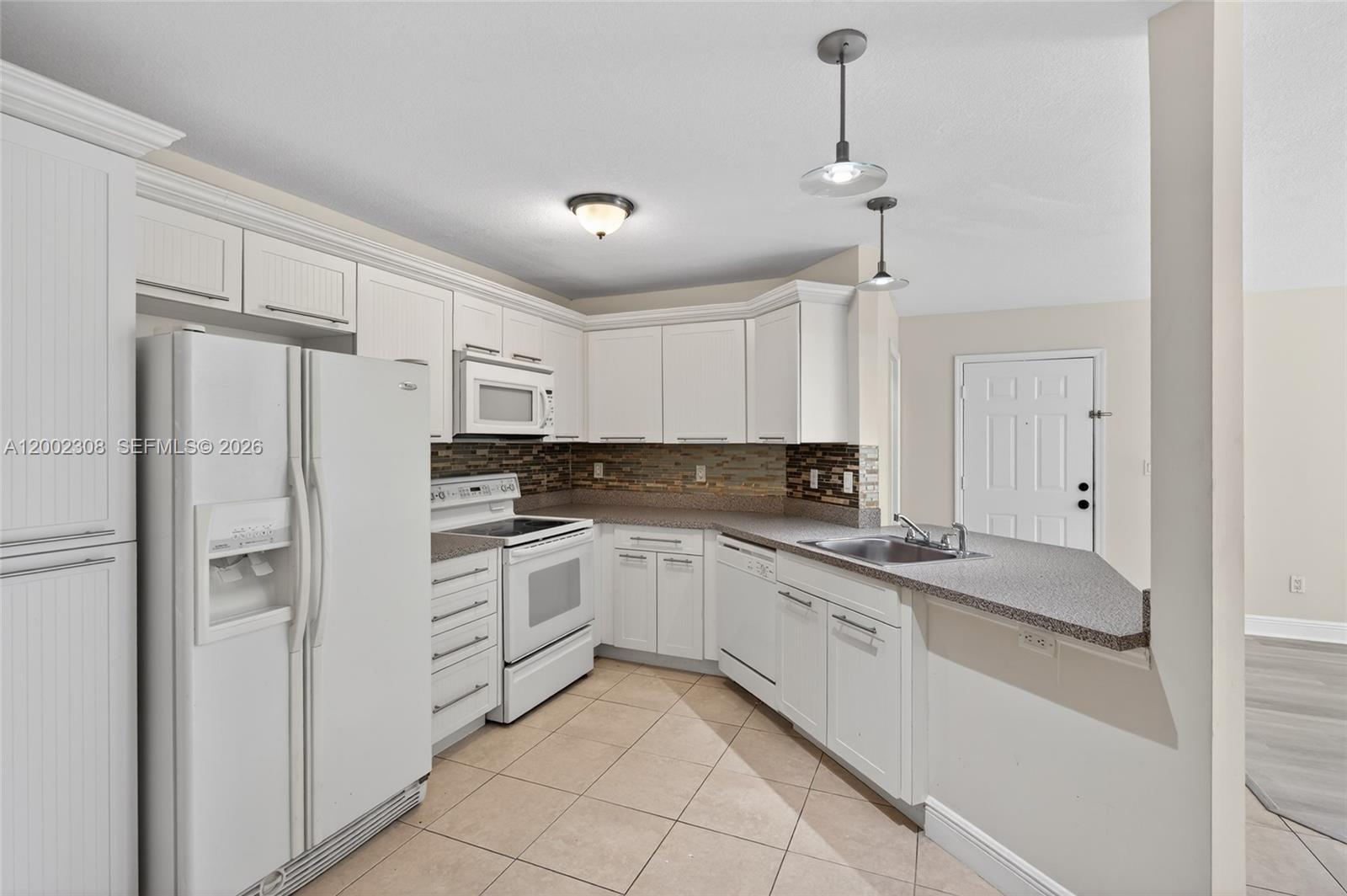 A kitchen features white cabinets, granite countertops, a tiled backsplash, and white appliances — 4025 W Mcnab Rd # E109, Pompano Beach FL 33069, POMPANO BEACH, FL