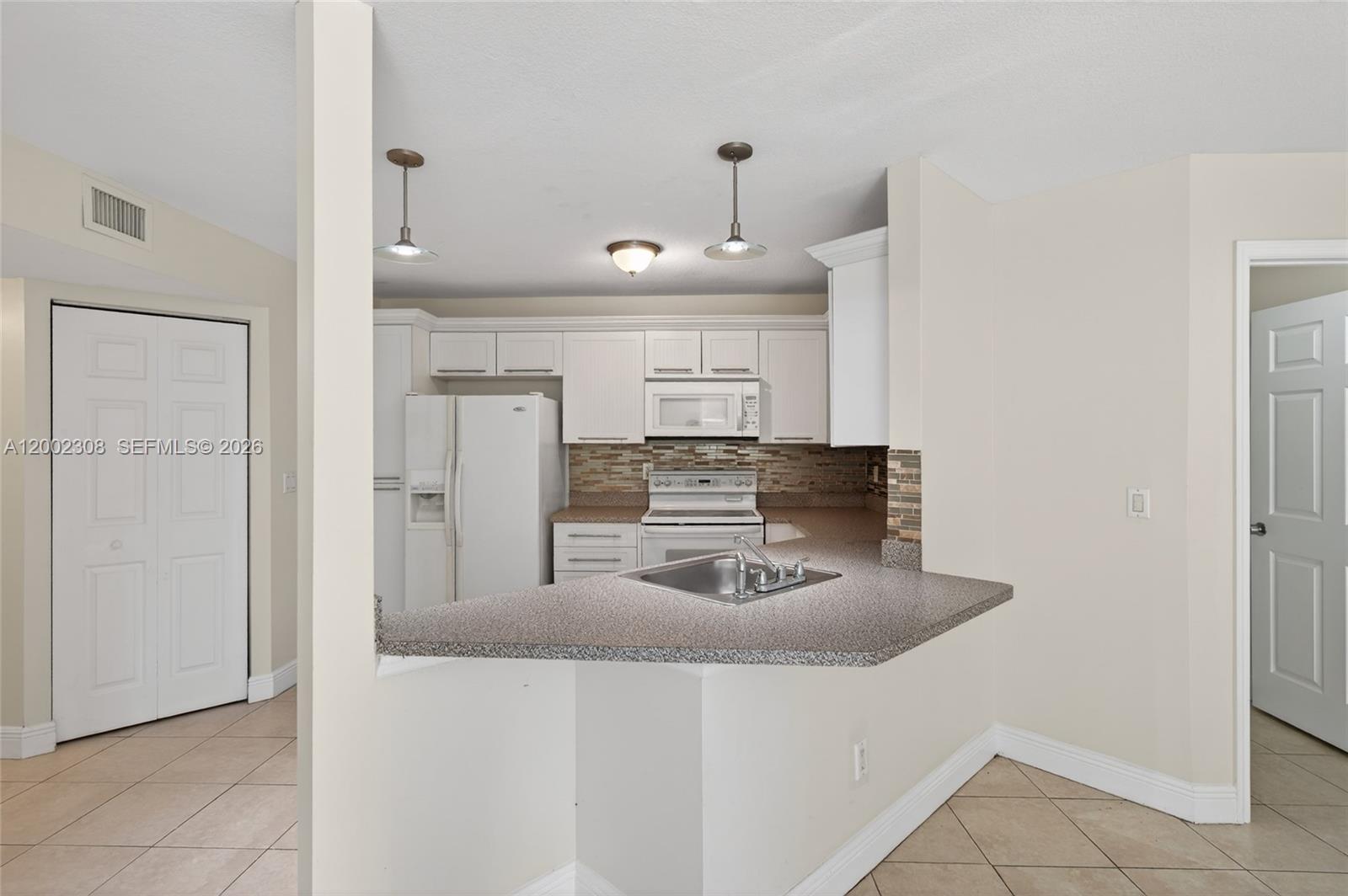 A kitchen features white cabinetry, a speckled countertop, a tiled backsplash, and a breakfast bar — 4025 W Mcnab Rd # E109, Pompano Beach FL 33069, POMPANO BEACH, FL