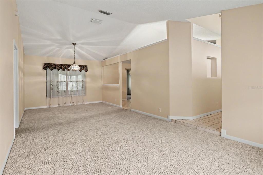 A carpeted living room with a vaulted ceiling, a chandelier, and a tiled entryway — 875 GABRIEL AVENUE NE, PALM BAY, FL