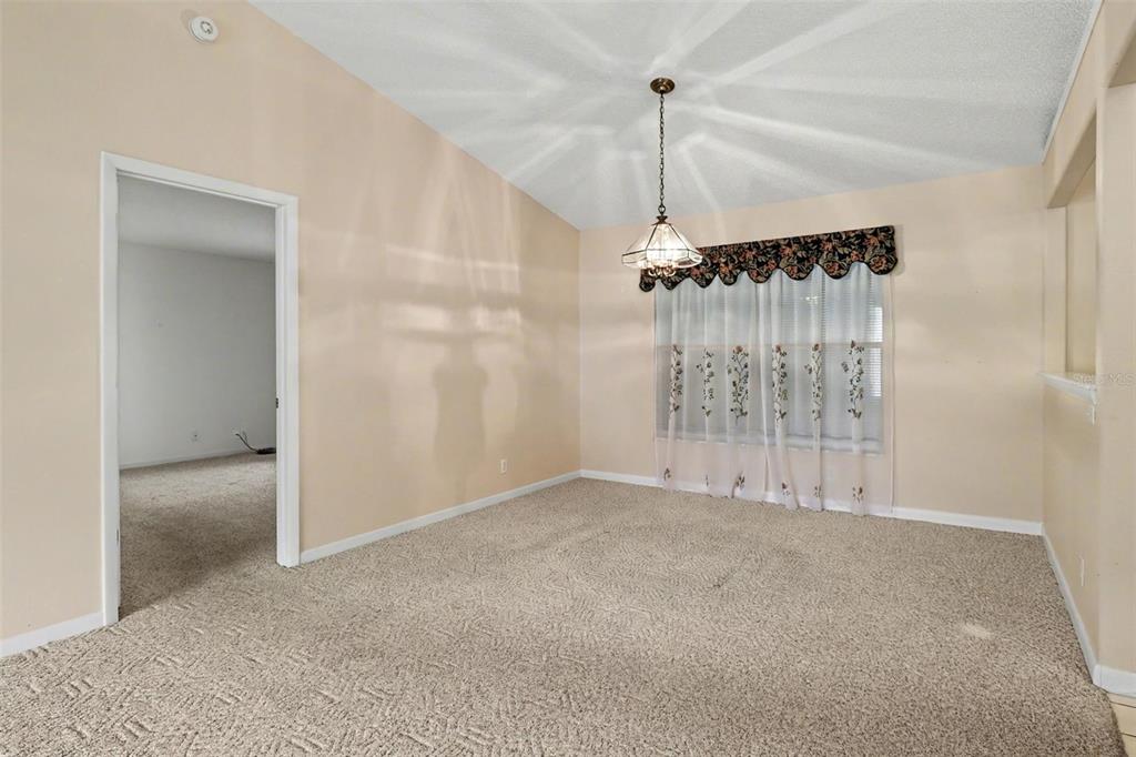 A dining room with beige carpet, a vaulted ceiling, a chandelier, and floral-patterned window curtains — 875 GABRIEL AVENUE NE, PALM BAY, FL