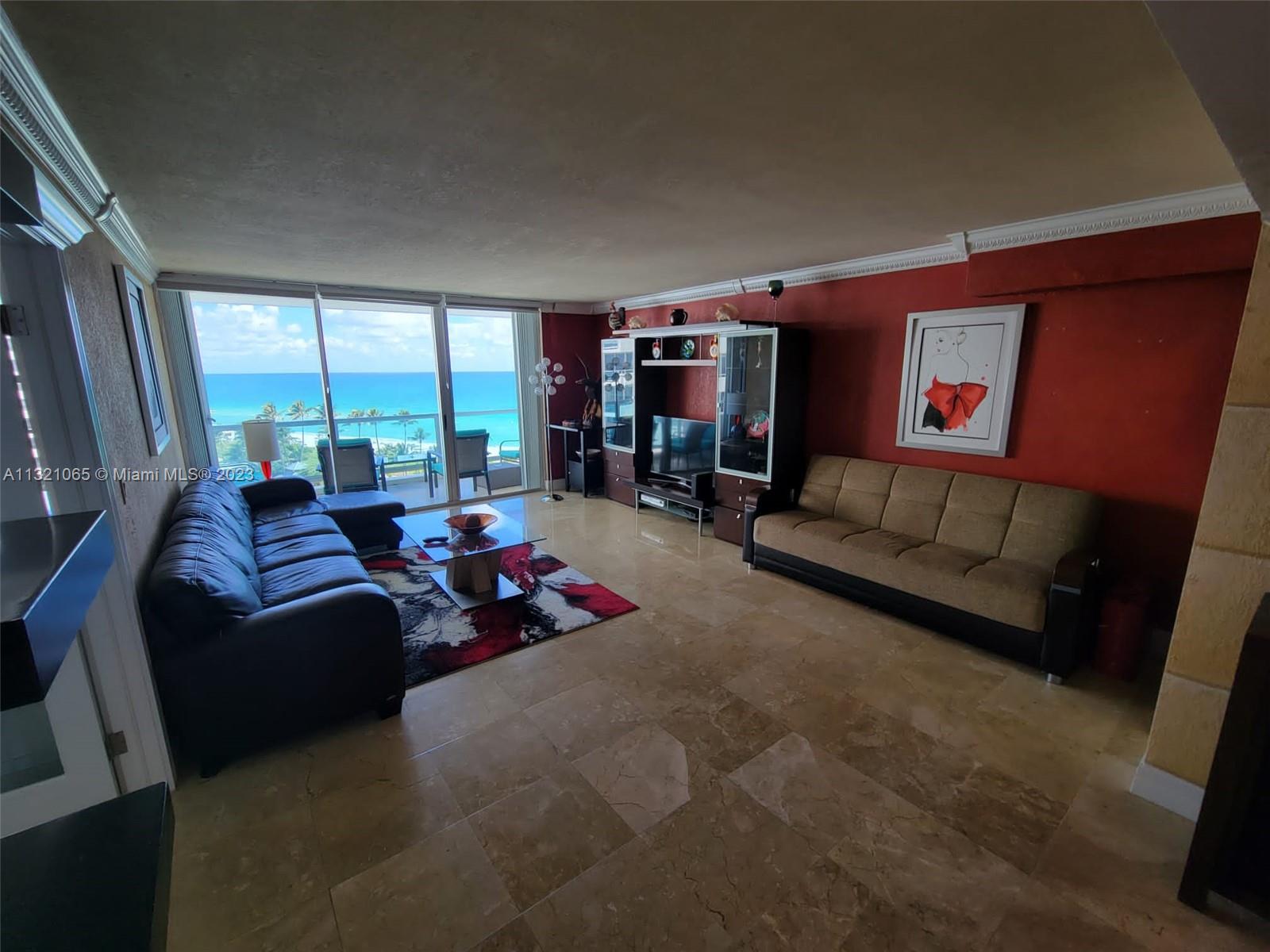 A living room features a red accent wall, tile flooring, and floor-to-ceiling ocean view windows — 5151 Collins Ave # 1036, Miami Beach FL 33140, MIAMI BEACH, FL