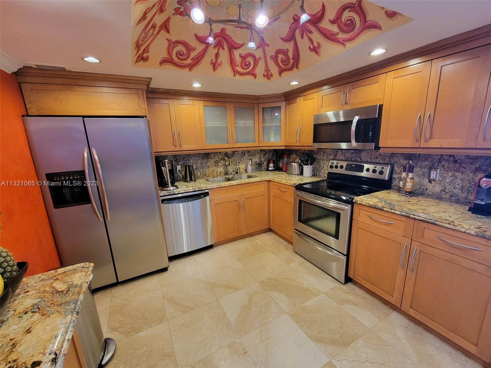 A kitchen features light wood cabinets, stainless steel appliances, granite countertops, and a painted ceiling — 5151 Collins Ave # 1036, Miami Beach FL 33140, MIAMI BEACH, FL