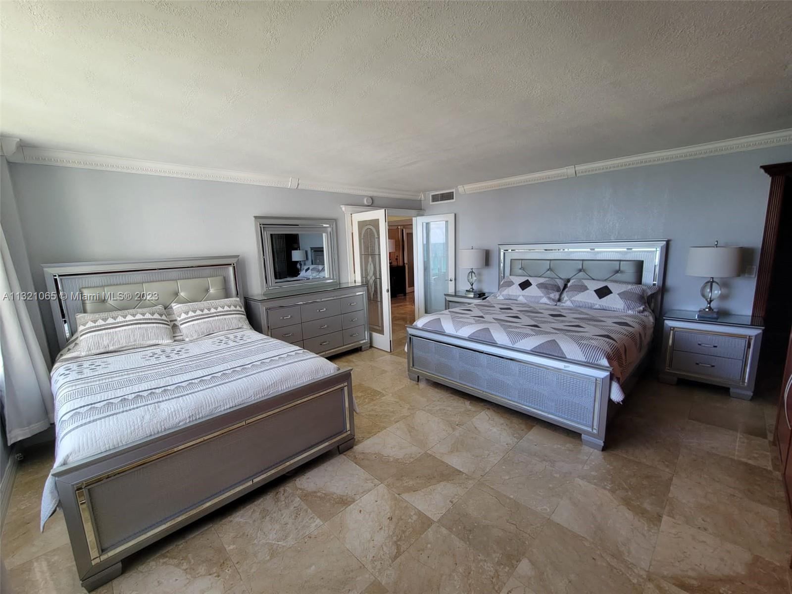 A bedroom features two large beds, a dresser with a mirror, and tile flooring — 5151 Collins Ave # 1036, Miami Beach FL 33140, MIAMI BEACH, FL
