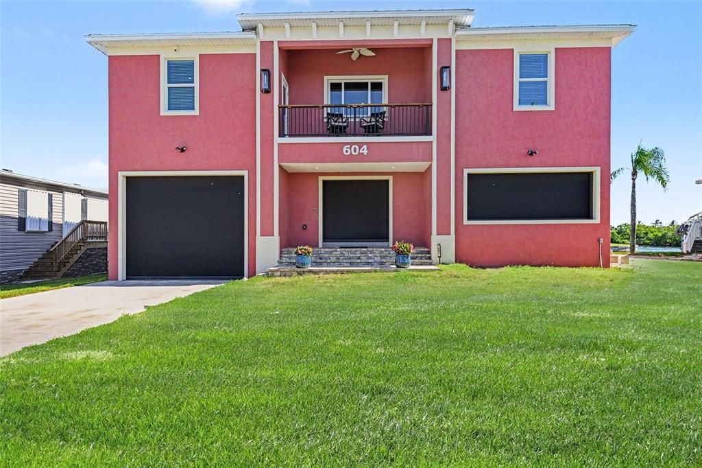 A pink two-story house features a garage, a second-floor balcony, and dark window shutters — 604 TAHITI COURT, PUNTA GORDA, FL