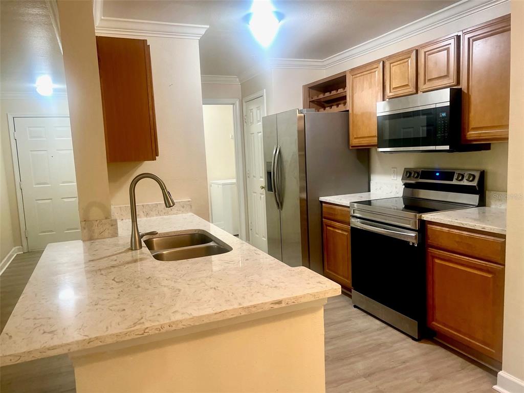 A kitchen features a stone-topped island with a sink, stainless steel appliances, and wood cabinets — 18335 BRIDLE CLUB DRIVE UNIT 18335, TAMPA, FL
